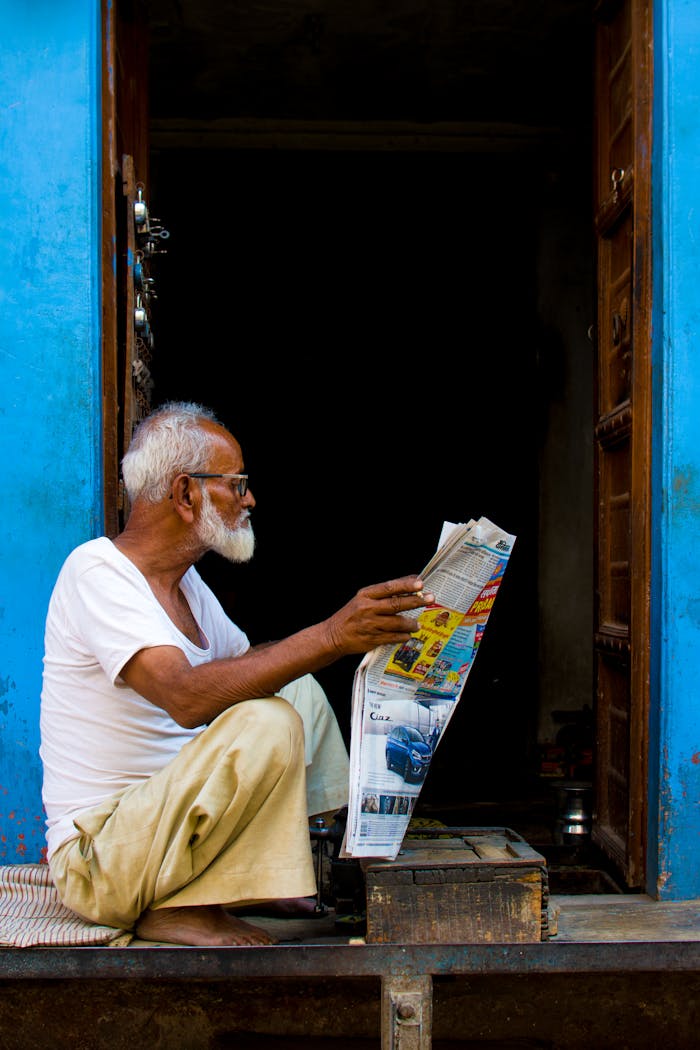 Old Man Sitting While Holding Newspaper Article